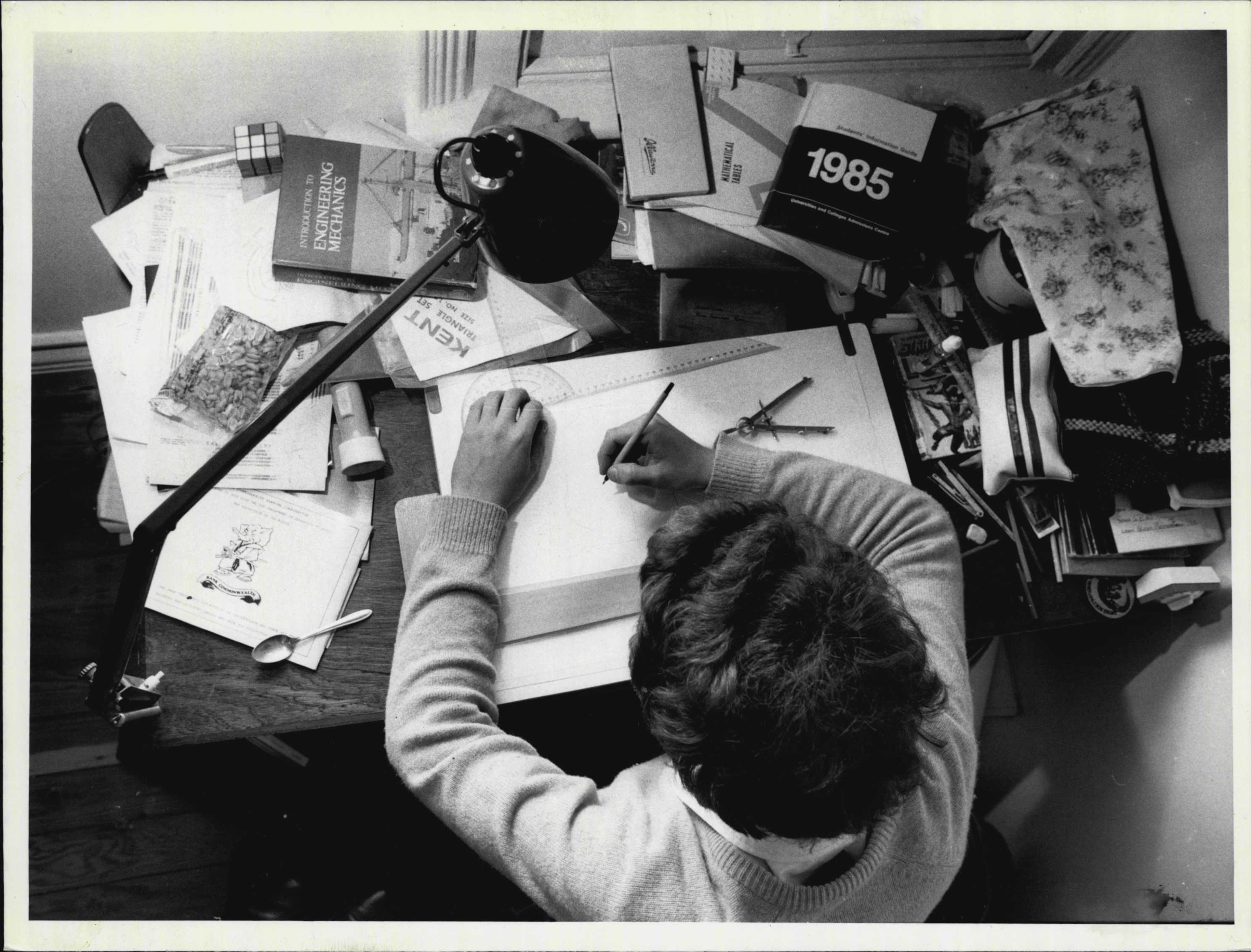 A person sits at a desk filled with books and writes in a notebook.