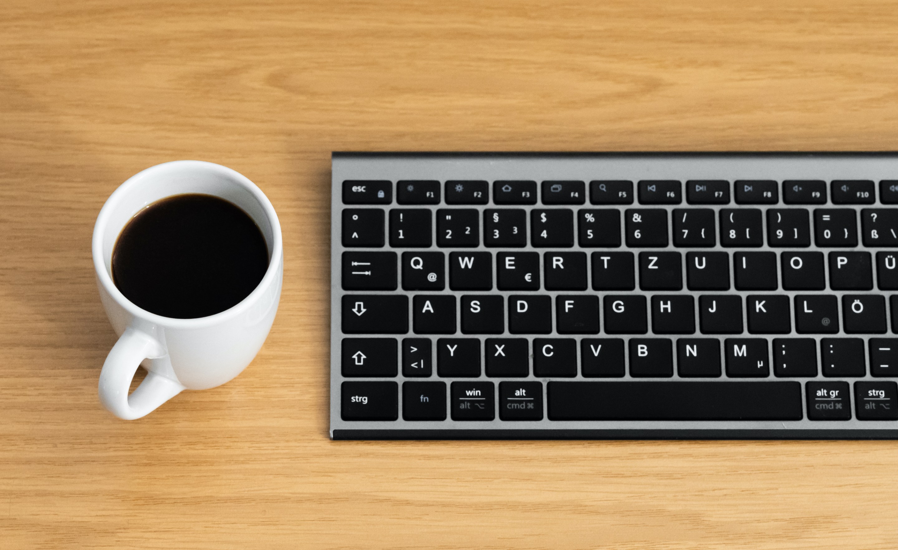 A mug of coffee next to a keyboard.