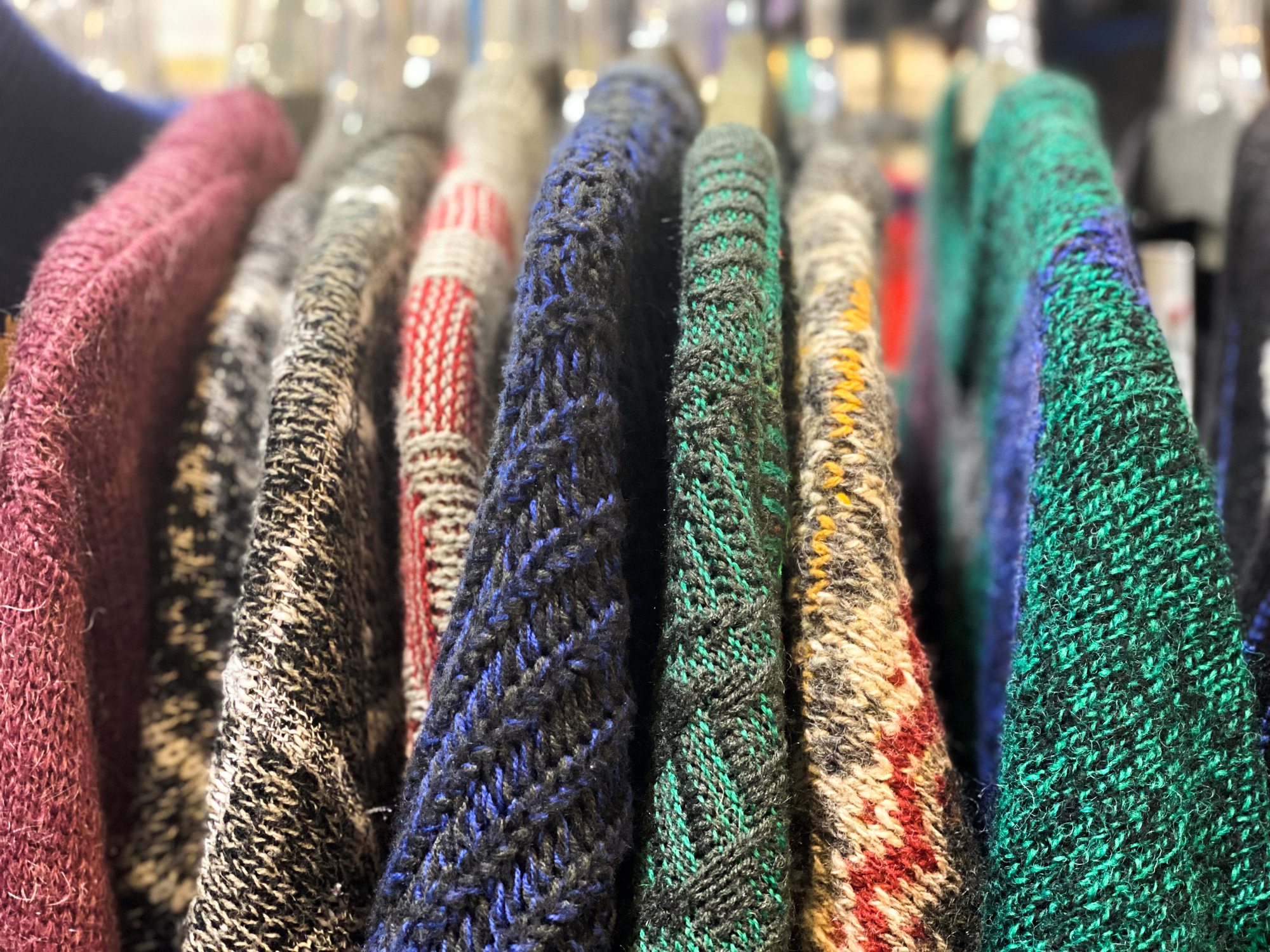 A clothing rack at a flea market showing a row of vintage sweaters of various colors.