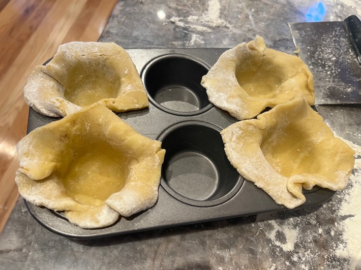 Raw tart dough shaped to the sides of muffin cups, and then rested inside a muffin tin.