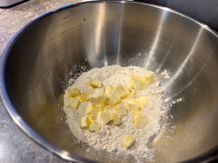 Flour and cubed butter sit in the bottom of a large metal mixing bowl.