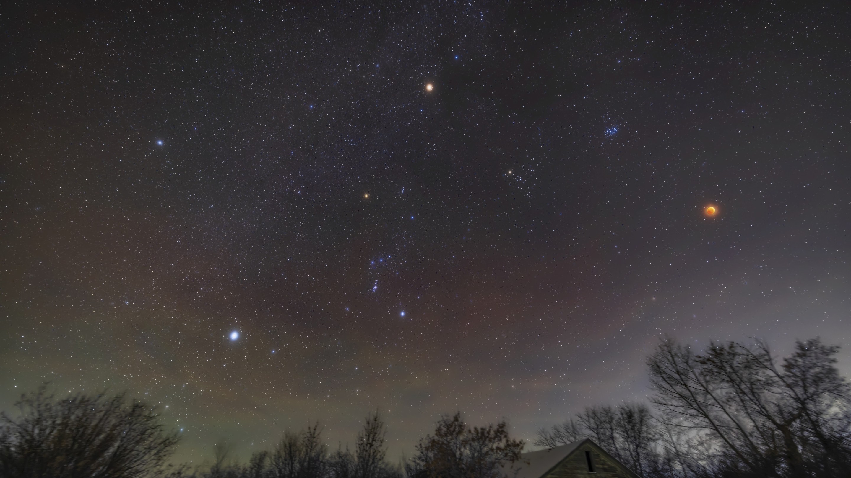 A wide-angle view of the total eclipse of the Moon of November 8, 2022, with the red Moon at right amid the stars of the northern winter sky and Milky Way, plus with bright red Mars at top. Above and left of the Moon is the blue Pleiades star cluster, while below it and to the left is the larger Hyades cluster with reddish Aldebaran in Taurus. The stars of Orion are left of centre, including reddish Betelgeuse, while at far left are the two Dog Stars: Procyon, at top, in Canis Minor, and Sirius, at bottom, in Canis Major. So this is a gathering of many red stars, planets and the rare red Moon. I shot the frames for this scene beginning at 3:50 am MST, 10 minutes before mid-totality during this 1h25m-long total eclipse. . (Photo by: Alan Dyer/VW Pics/Universal Images Group via Getty Images)