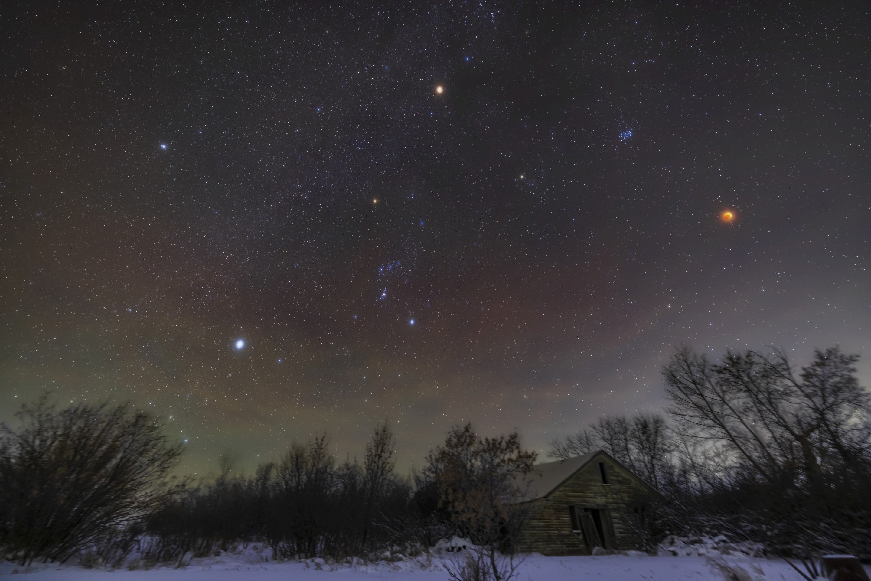 A wide-angle view of the total eclipse of the Moon of November 8, 2022, with the red Moon at right amid the stars of the northern winter sky and Milky Way, plus with bright red Mars at top. Above and left of the Moon is the blue Pleiades star cluster, while below it and to the left is the larger Hyades cluster with reddish Aldebaran in Taurus. The stars of Orion are left of centre, including reddish Betelgeuse, while at far left are the two Dog Stars: Procyon, at top, in Canis Minor, and Sirius, at bottom, in Canis Major. So this is a gathering of many red stars, planets and the rare red Moon. I shot the frames for this scene beginning at 3:50 am MST, 10 minutes before mid-totality during this 1h25m-long total eclipse. . (Photo by: Alan Dyer/VW Pics/Universal Images Group via Getty Images)