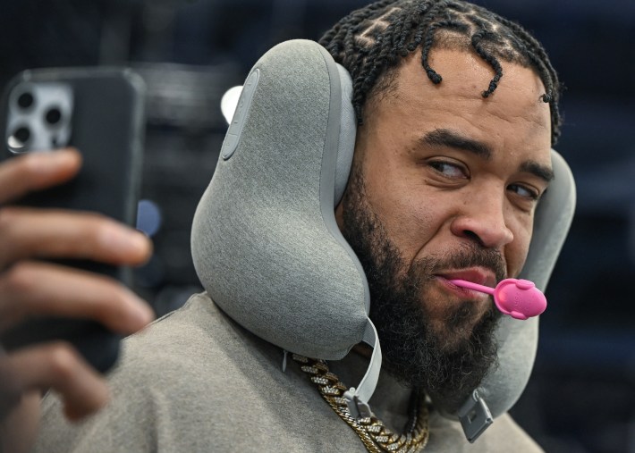 JaVale McGee taking a selfie of himself with a lollipop of some kind in his mouth and some kind of headphone thing on his head at CES.