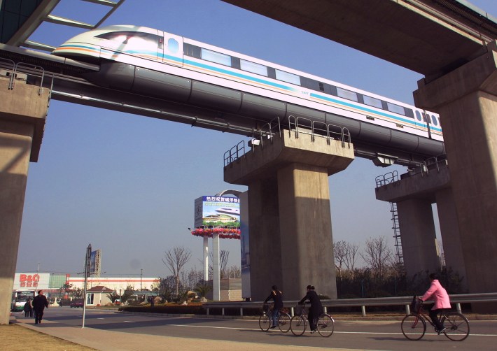 The Shanghai Transrapid maglev train passes over a road with cyclists in Shanghai, China.