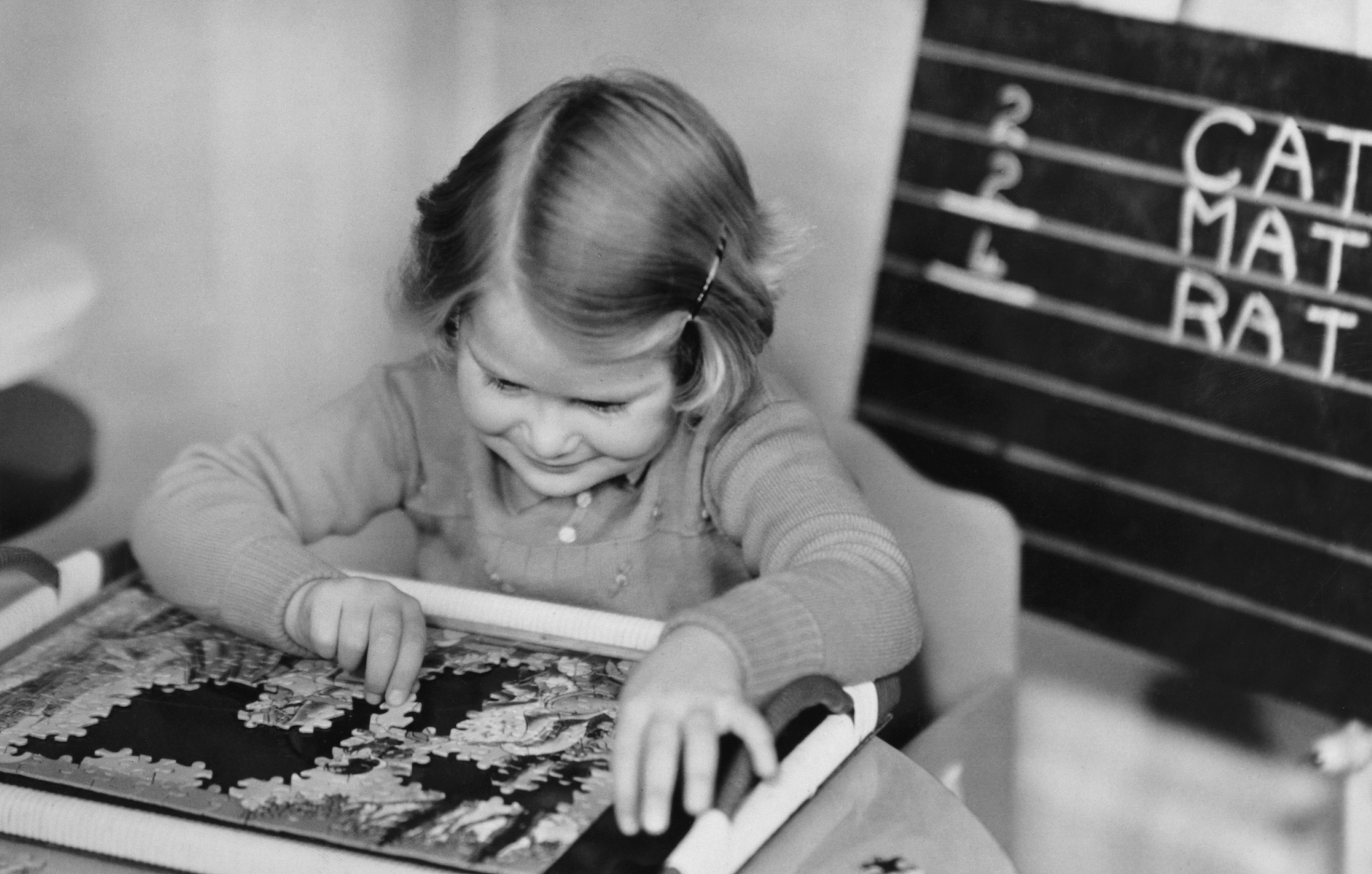 A little girl completes a jigsaw puzzle delivered to her by Santa Claus, 24th December 1938.