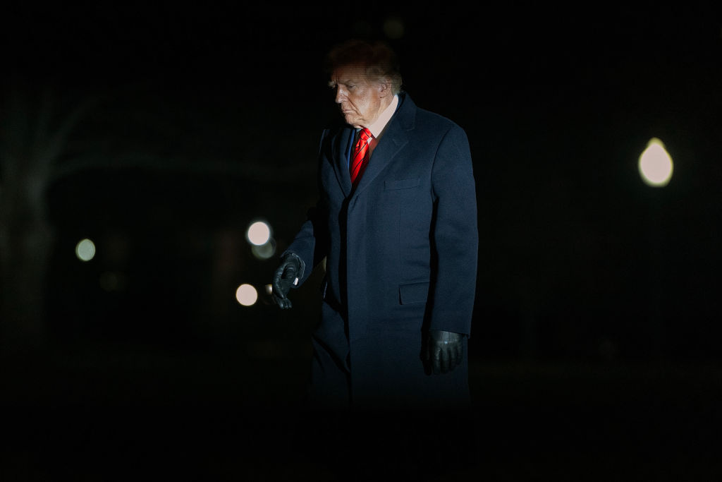 President Trump walks across the south lawn of the White House in a black coat after returning from a trip