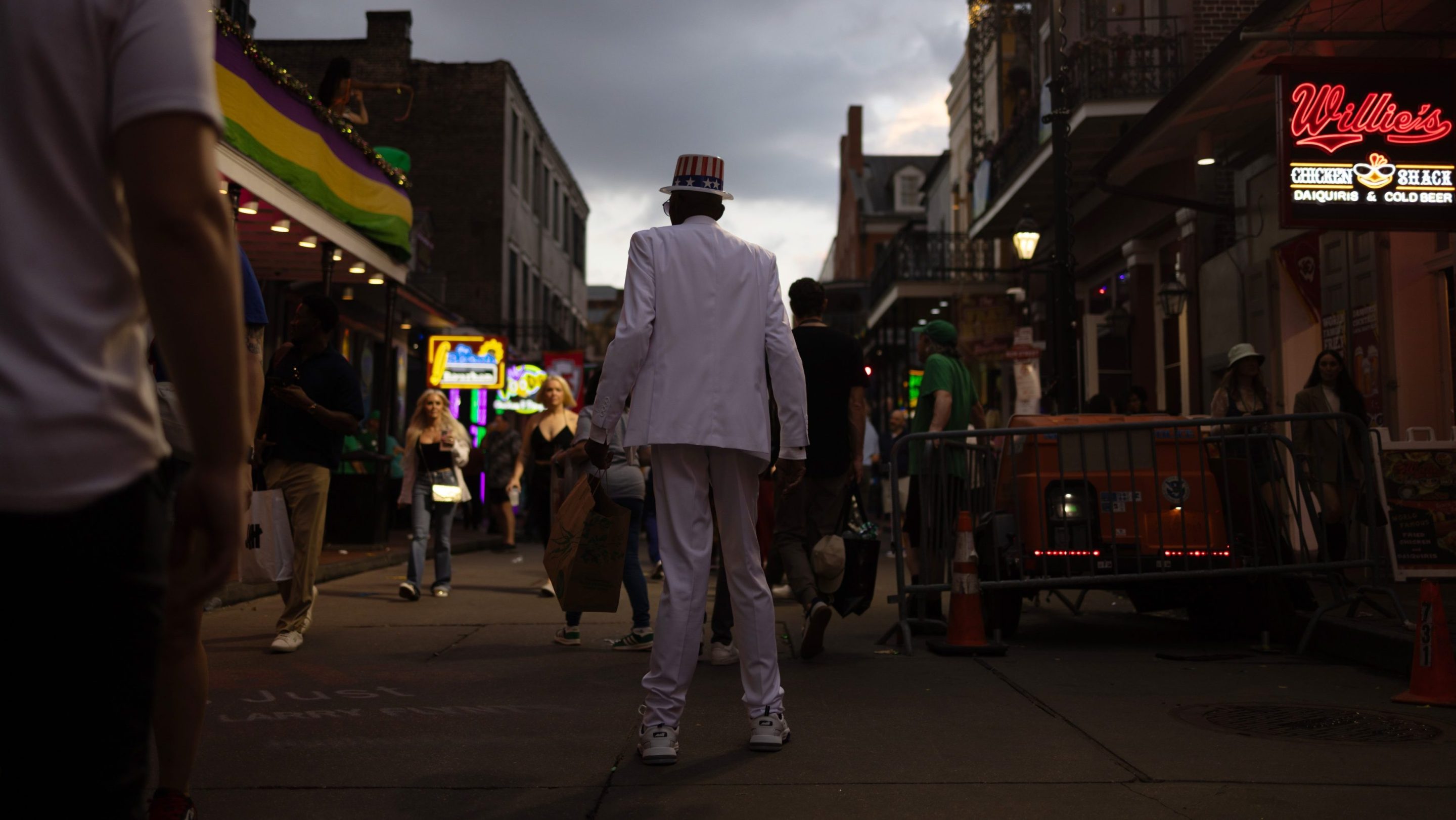 A photo of a man on stilted legs and dressed in white suit walking down a dark and mostly empty Bourbon Street in New Orleans.