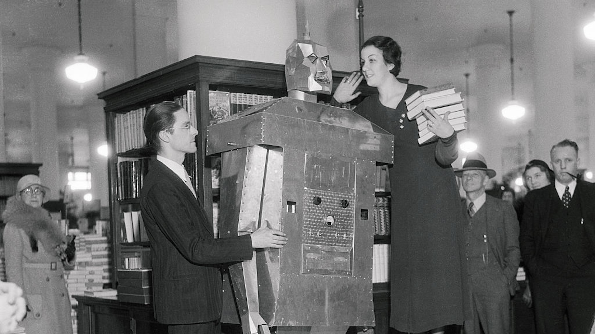 An Adventure Story? Miss Betty Davis tries out her sales talk on the robot invented by Eark Kent, (left), of Carthage, Missouri, in the May Company Store in Los Angeles. The 21-year-old inventor claims that "John" walks, smokes cigarettes, spits fire, and gets generally "het up" when he doesn't receive attention.