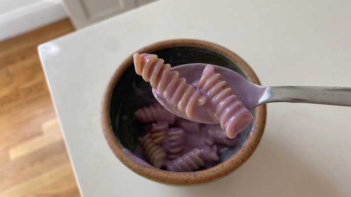 Uma pequena tigela de macarrão Rotini girou em iogurte de soja de mirtilo de cor roxa