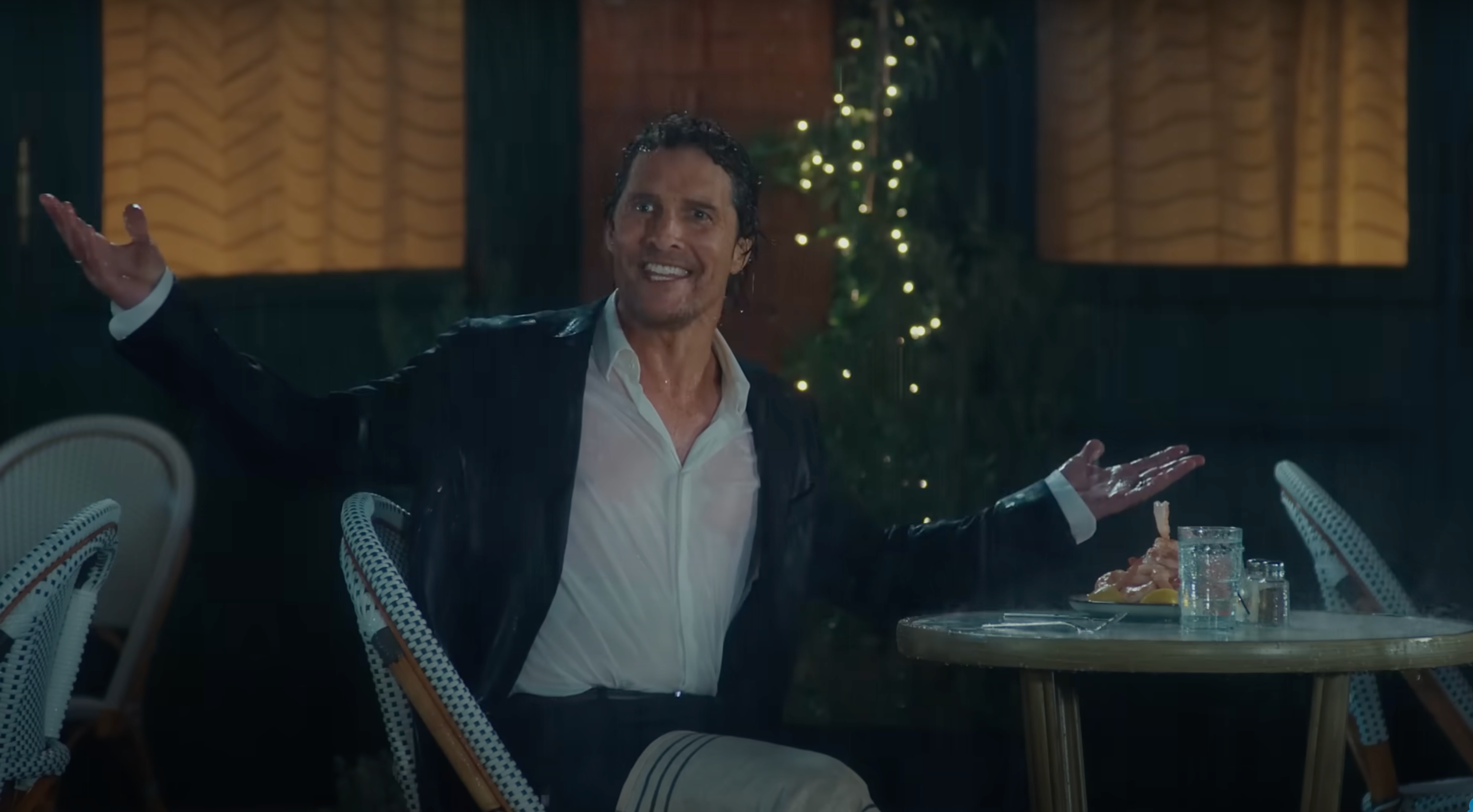 The actor Matthew McConaughey looking slightly deranged while sitting at an outdoor restaurant table, in the dark, under a torrential downpour.