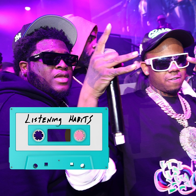 NEW YORK, NEW YORK - DECEMBER 28: Cash Cobain and Bay Swag attend Funk Flex Winter Fest on December 28, 2024 in New York City. Cobain is wearing a Yankees cap and sunglasses. He has a beard that's short and hit shis chin. He's in a blue hoodie. Bay Wag is wearing a big gold chain, sunglasses, a baseball hat, a very diamond-encrusted watch, and holding a plastic bottle of water in one hand and a microphone in the other