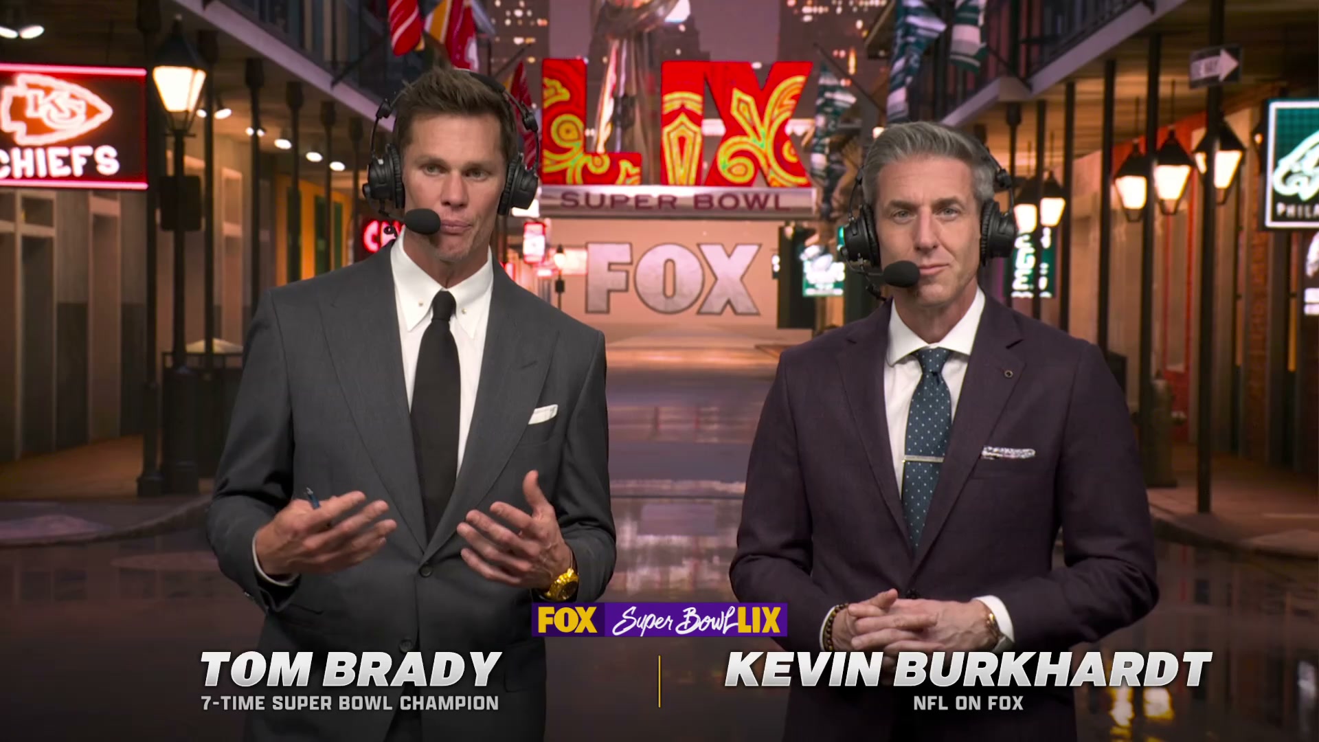 Tom Brady and Kevin Burkhardt in front of a green screen that looks like a deserted alleyway.