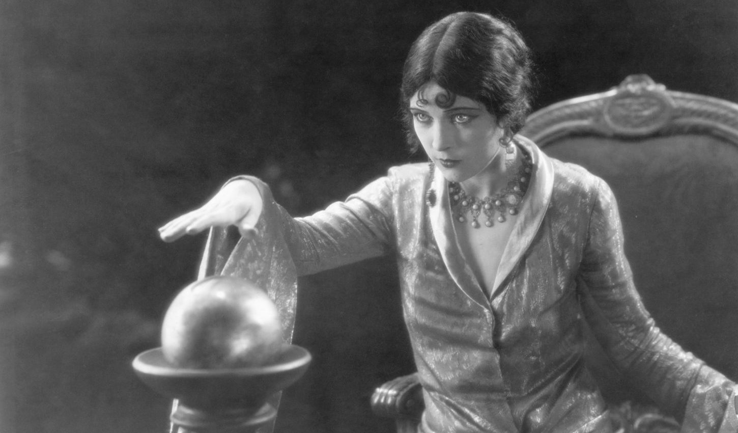 Woman holding her hand over a crystal ball and gazing into the future. Seated 1/2 length photograph.