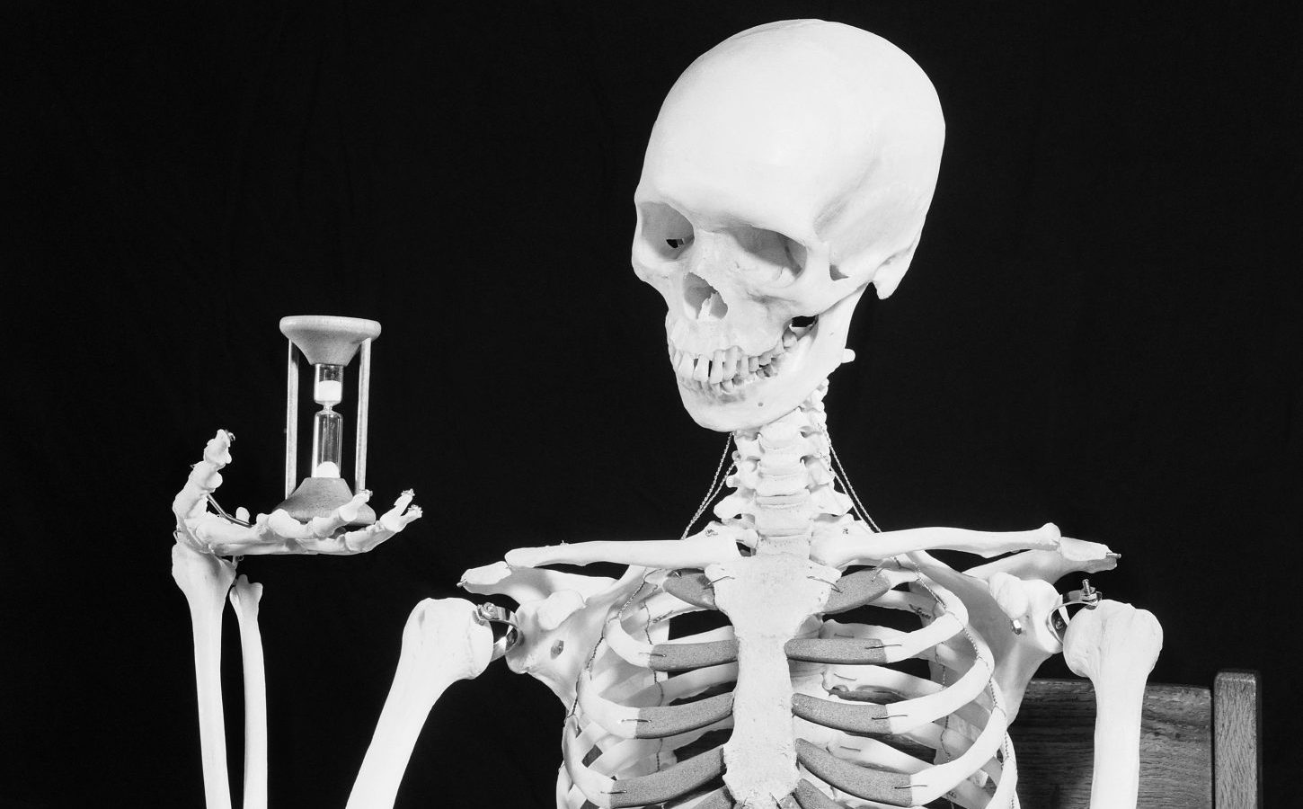 Skeleton seated at a table, holding an hourglass. Undated photograph.