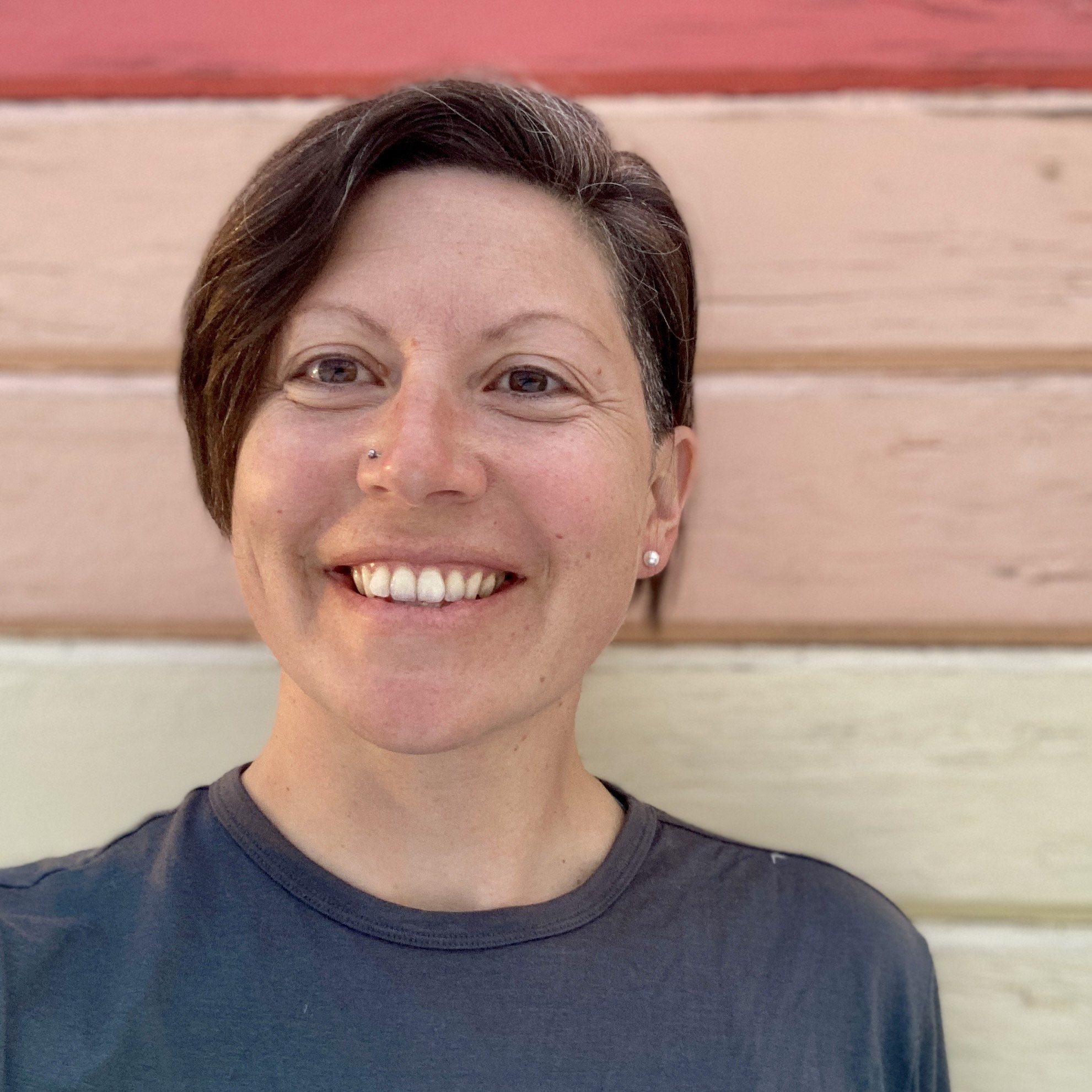 a photo of Kate Wheeler, a former USDA farm to school specialist. Kate has short brown hair and is smiling in front of several painted planks