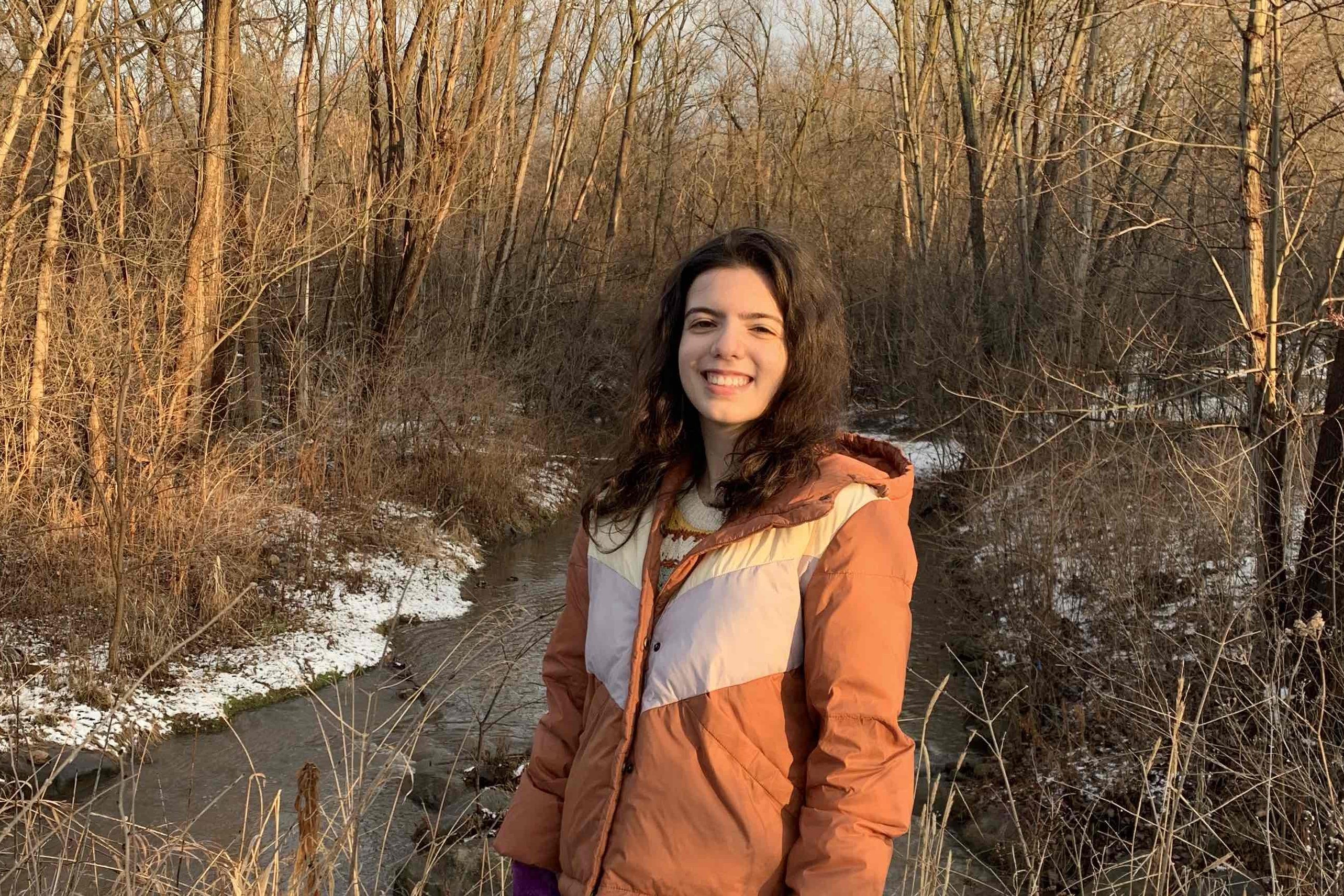 a photo of Veronica Correa, a fired EPA public affairs specialist, standing in snowy woods by a stream