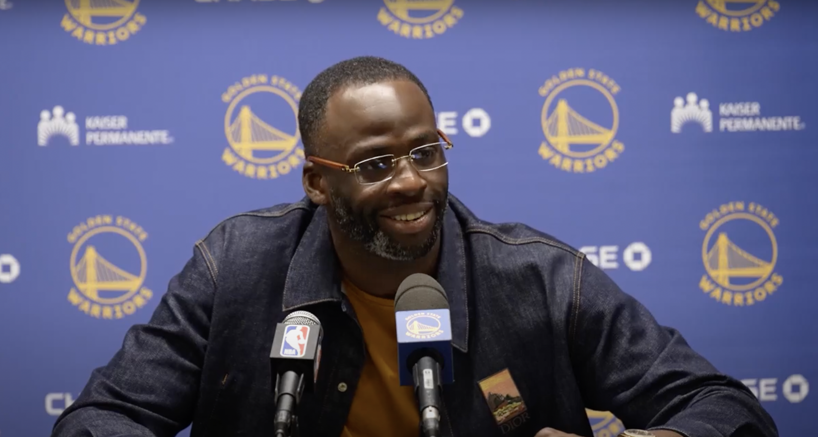 Draymond Green smiles at a press conference after being told that Karl-Anthony Towns did not miss a game because he was scared of Jimmy Butler, per Green's speculation, but because of the death of a family friend