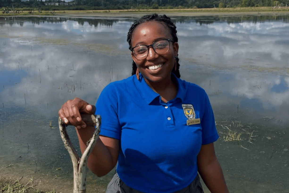 a photo of Kaesee Bourne, a former fish and wildlife biologist at the USFWS, holding a shovel in front of a wetland