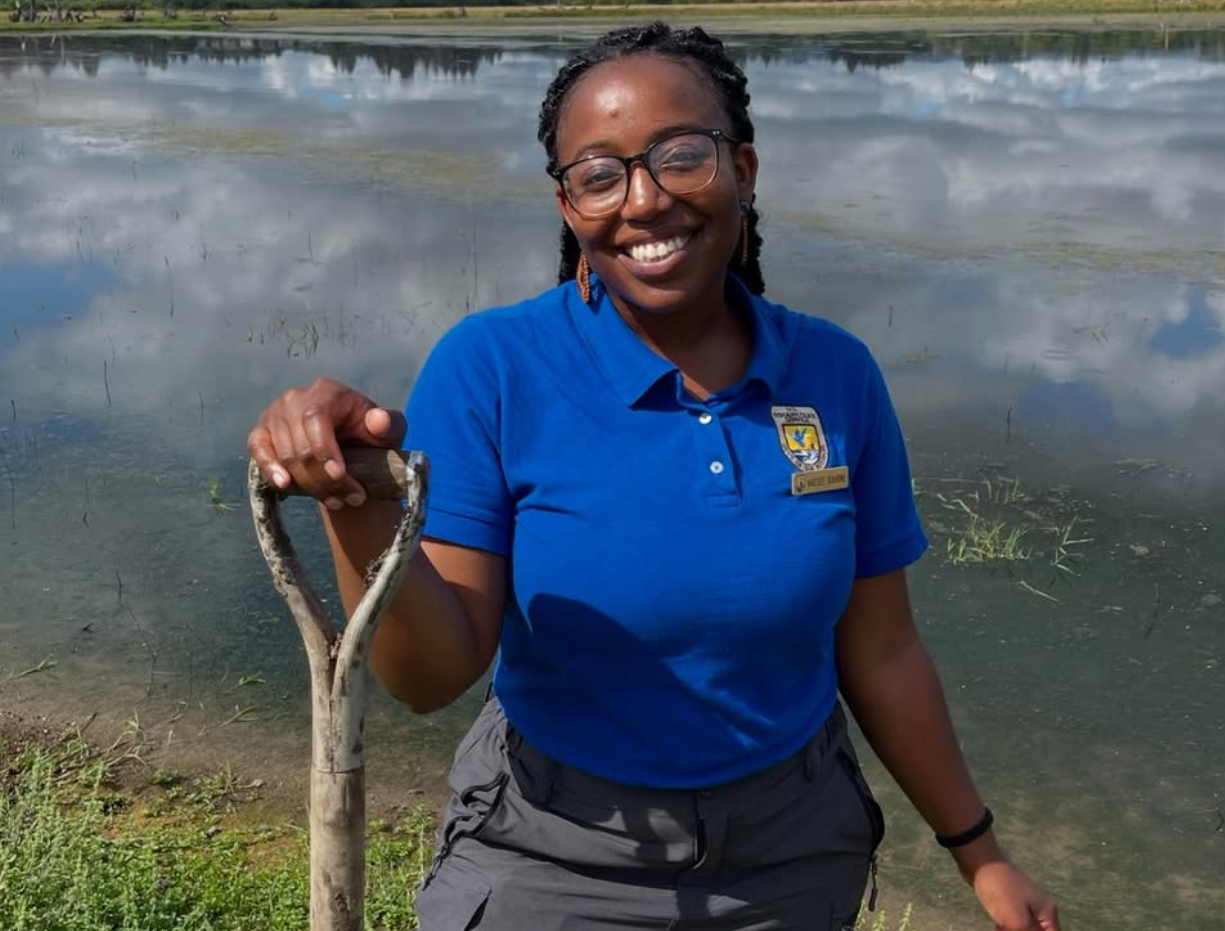 a photo of Kaesee Bourne, a former fish and wildlife biologist at the USFWS, holding a shovel in front of a wetland