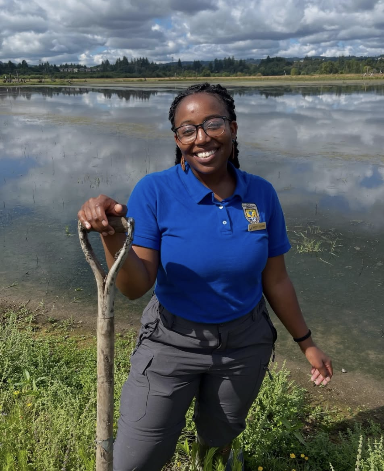 a photo of Kaesee Bourne, a former fish and wildlife biologist at the USFWS, holding a shovel in front of a wetland