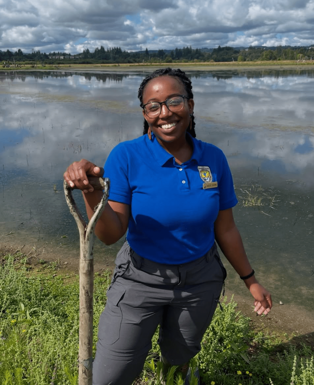 a photo of Kaesee Bourne, a former fish and wildlife biologist at the USFWS, holding a shovel in front of a wetland