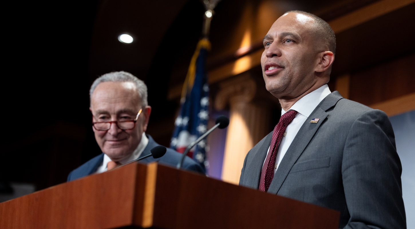 Senate minority leader Chuck Schumer and House minority leader Hakeem Jeffries, behind a podium at a press conference, looking like doofuses.