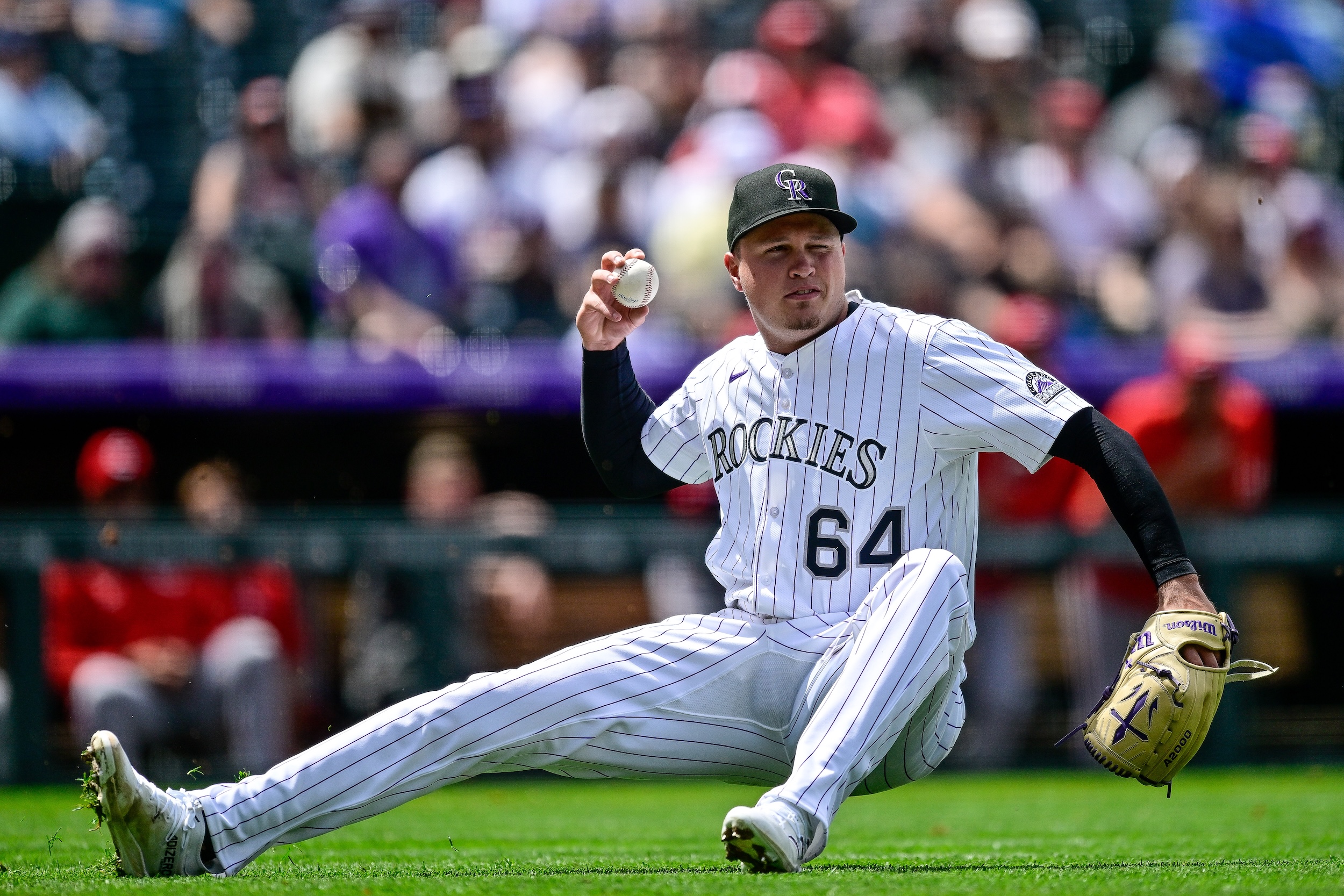 Bradley Blalock of the Rockies tries to throw a baseball while sliding on his butt.