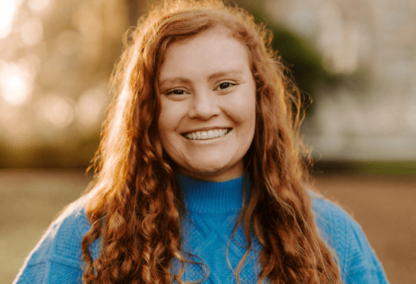 A headshot of Madyson Miller, a fired NOAA program analyst, in a blue sweater and golden light