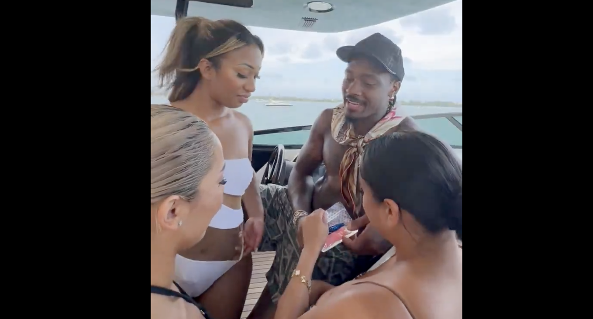 Stefon Diggs handing a pink substance to some women on a boat