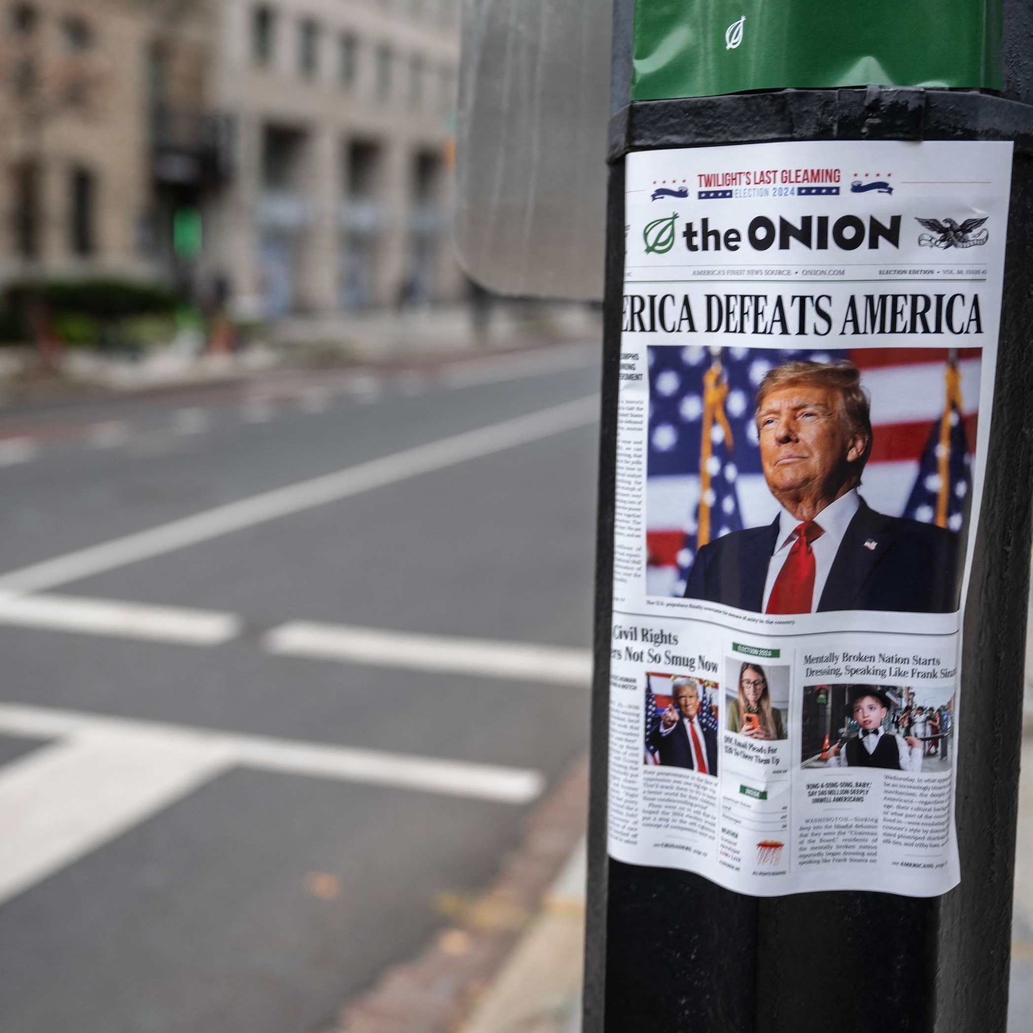 A copy of "The Onion," a satirical newspaper, is seen on a lamppost in downtown Washington, DC on November 14, 2024. The lead headline reads "America Defeats America."