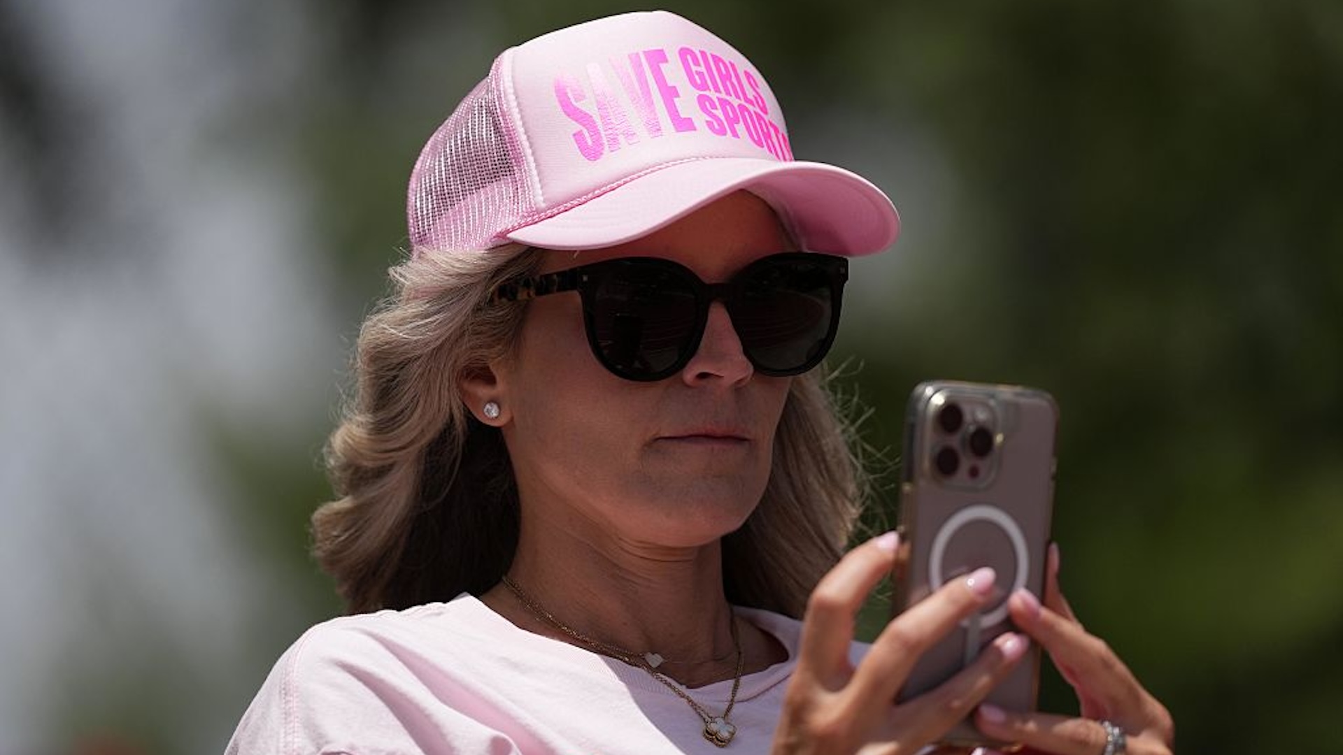 A woman wearing Save Girls Sport hat records a video of transgender athlete AB Hernandez of Jurupa Valley (not pictured) during the girls long jump at the CIF Southern Section Masters Meet at Moorpark High School on May 24, 2025 in Moorpark, California.
