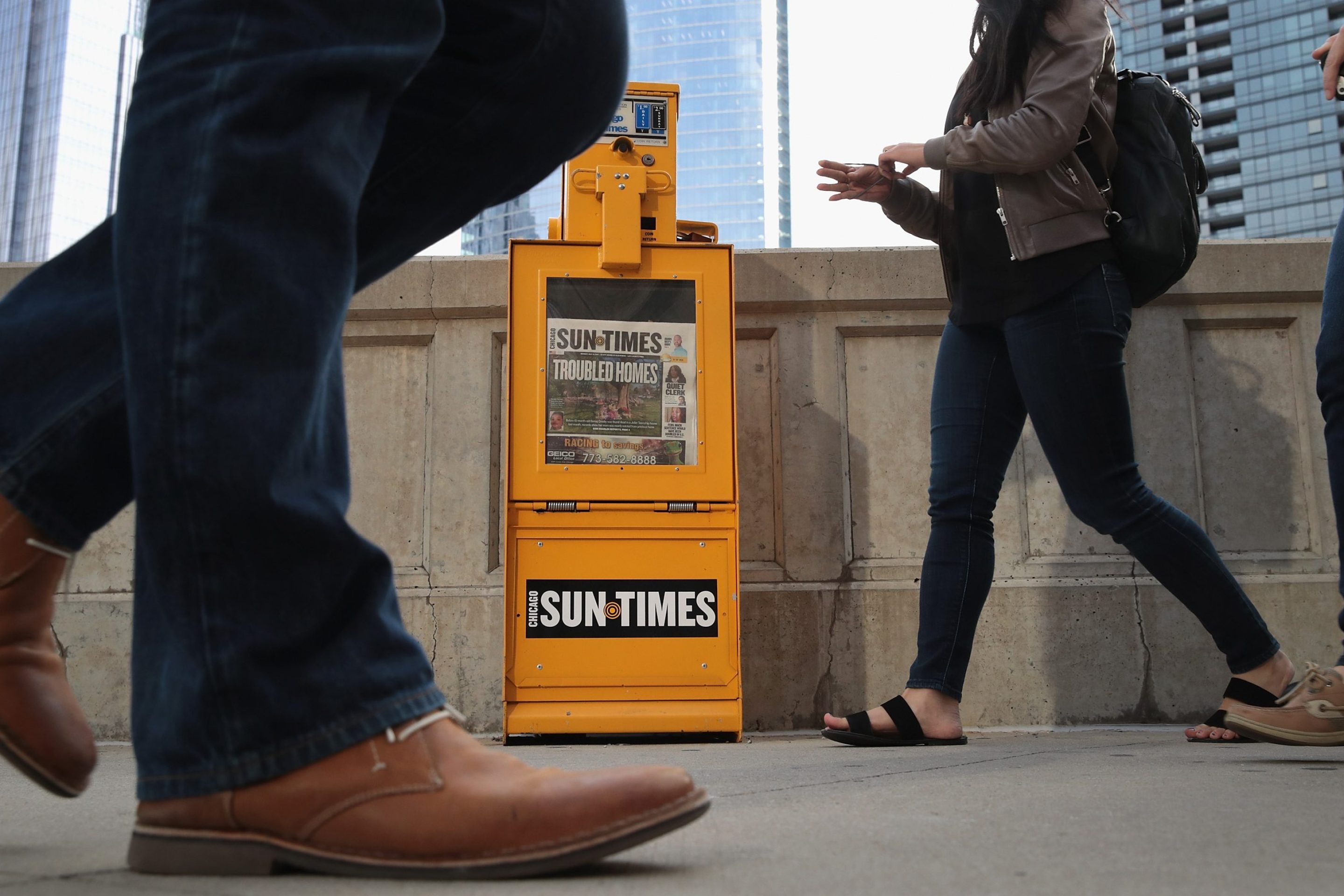 Chicago Sun Times newspapers are sold from of a dispenser near their editorial offices on May 15, 2017 in Chicago, Illinois. The box is yellow and people are walking around and in front of it.