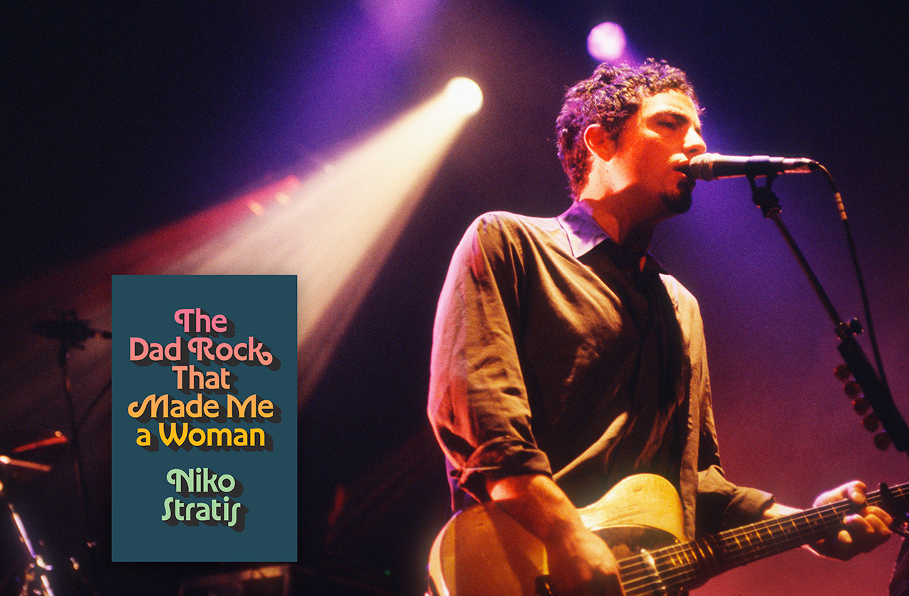 Jakob Dylan, in 1997, singing in front of a microphone. He has short curly hair, maybe has a little beard, and he's in a long sleeve collared button-front shirt. He's playing guitar. In the corner there's an image of a book cover: The Dad Rock That Made Me A Woman, by Niko Stratis