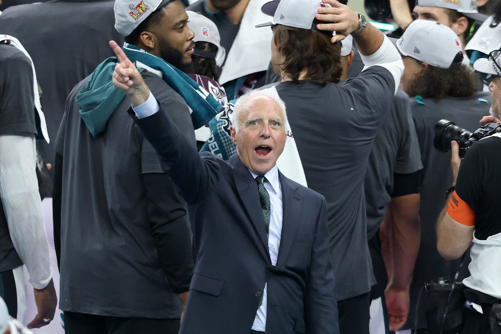 Jeffrey Lurie, in a suit and tie with Eagles players behind him, points to the sky with his mouth open in celebration after Super Bowl 59.