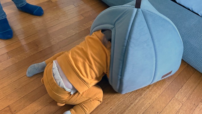 A toddler in Winnie the Pooh-colored sweatshirt and pants with his head in a grey yurt-like object that's supposed to be for a cat.