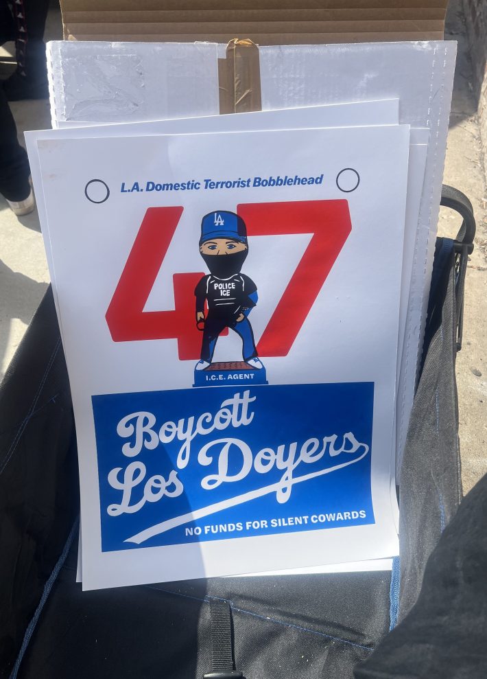 A protest sign at the Dodgers Protest. It reads, "L.A. Domestic Terrorist Bobblehead" and shows a Dodgers bobblehead dressed like an undercover ICE agent in front of the number 47. Below it reads, "Boycott Los Doyers no funds for silent cowards."