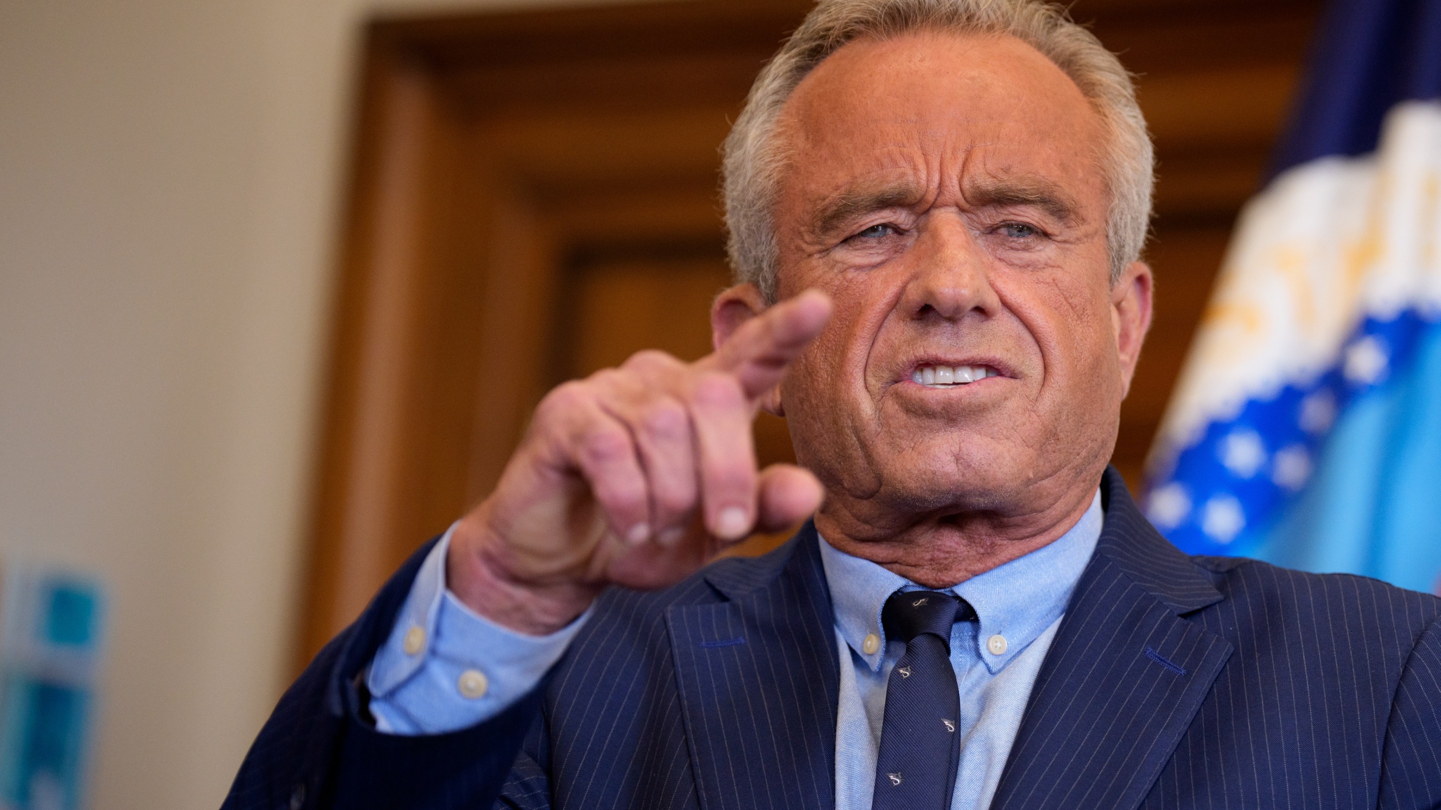 Health and Human Services Secretary Robert F. Kennedy Jr. speaks. He looks like a photographic negative and is grimacing. Skin the color of a hot dog.