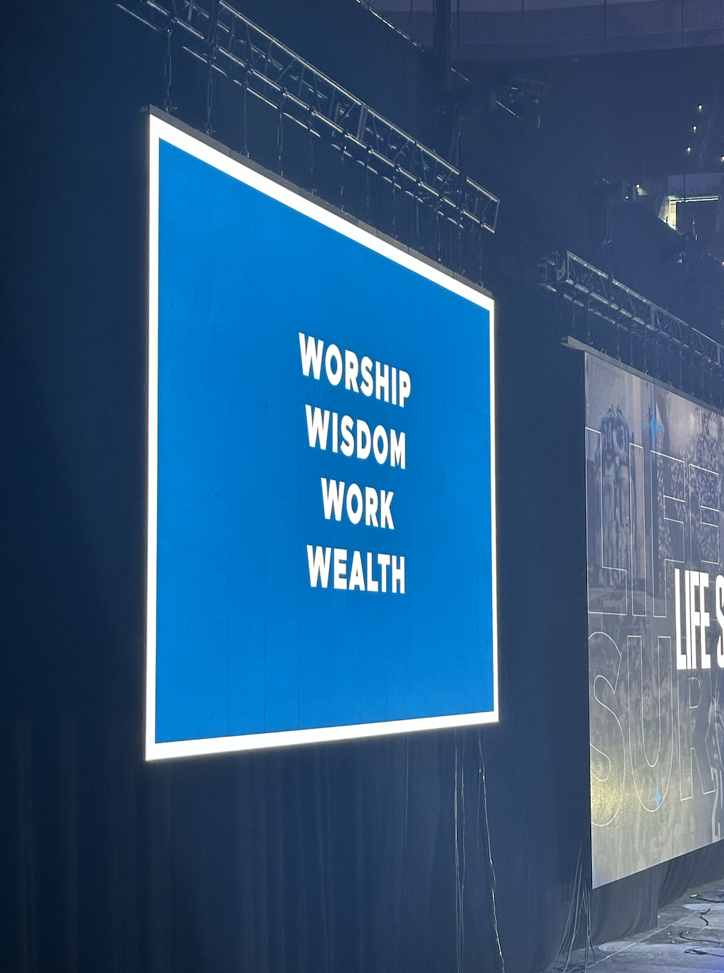 image of the screen at the Wells Fargo center displaying the words WORSHIP, WISDOM, WORK, WEALTH