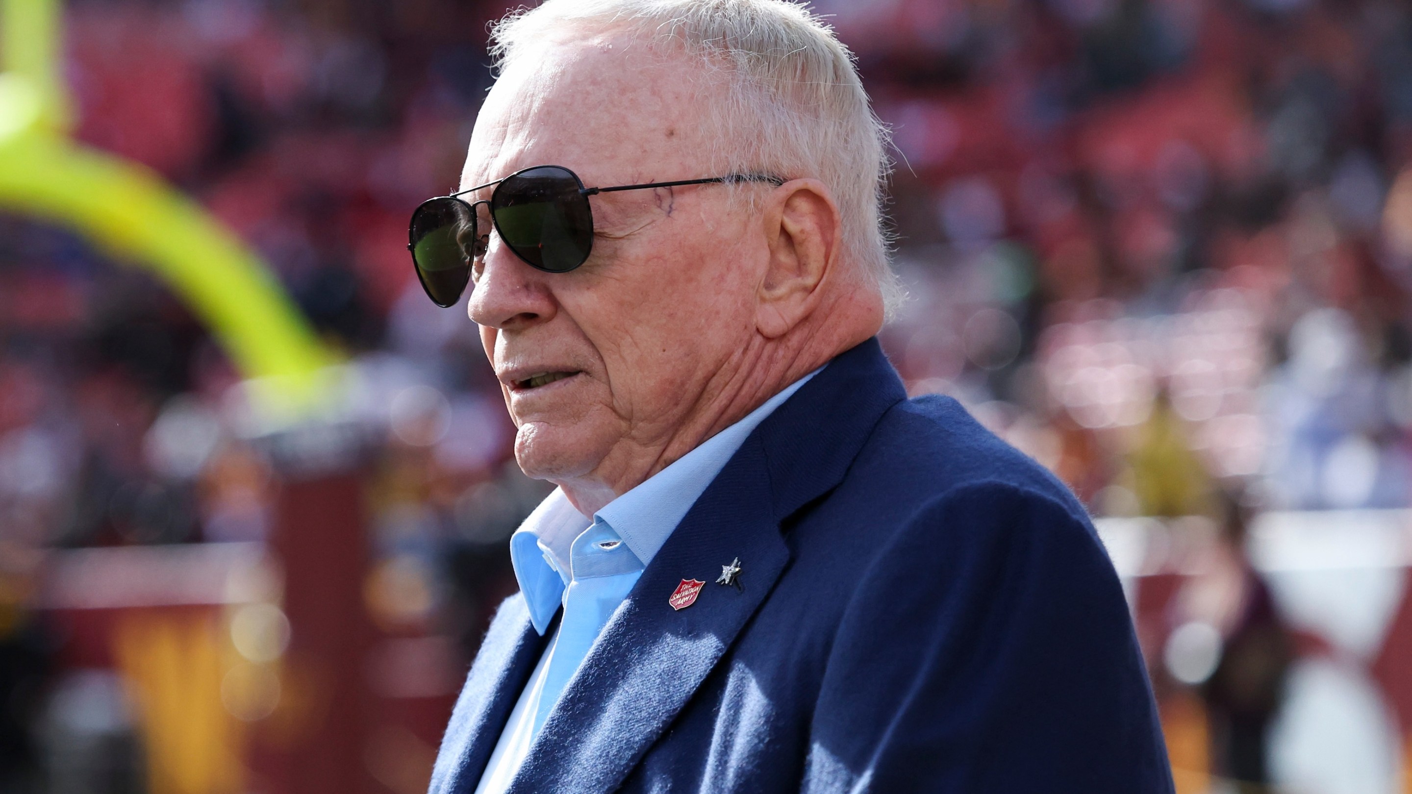 Jerry Jones, owner of the Dallas Cowboys, is seen on the field prior to a game against the Washington Commanders. His sunglasses are sitting in kind of a weird way, like hovering above his nose.