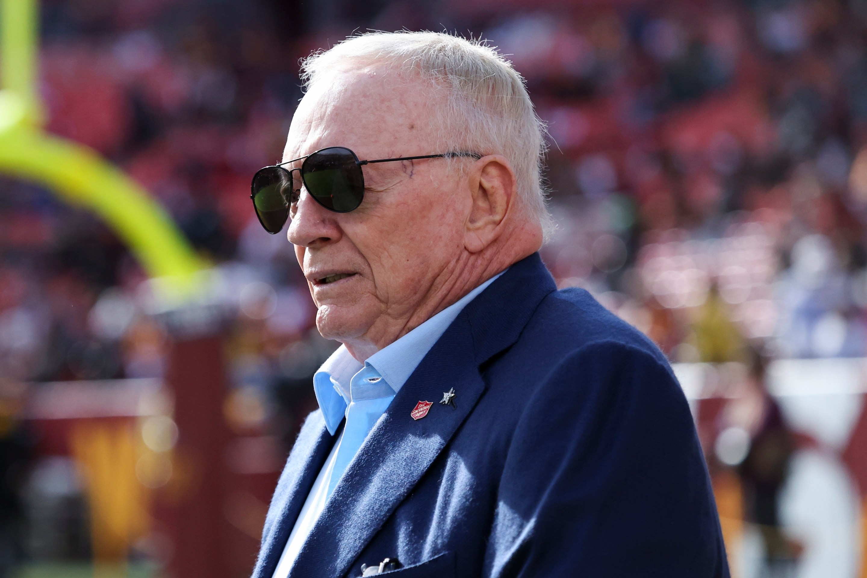 Jerry Jones, owner of the Dallas Cowboys, is seen on the field prior to a game against the Washington Commanders. His sunglasses are sitting in kind of a weird way, like hovering above his nose.