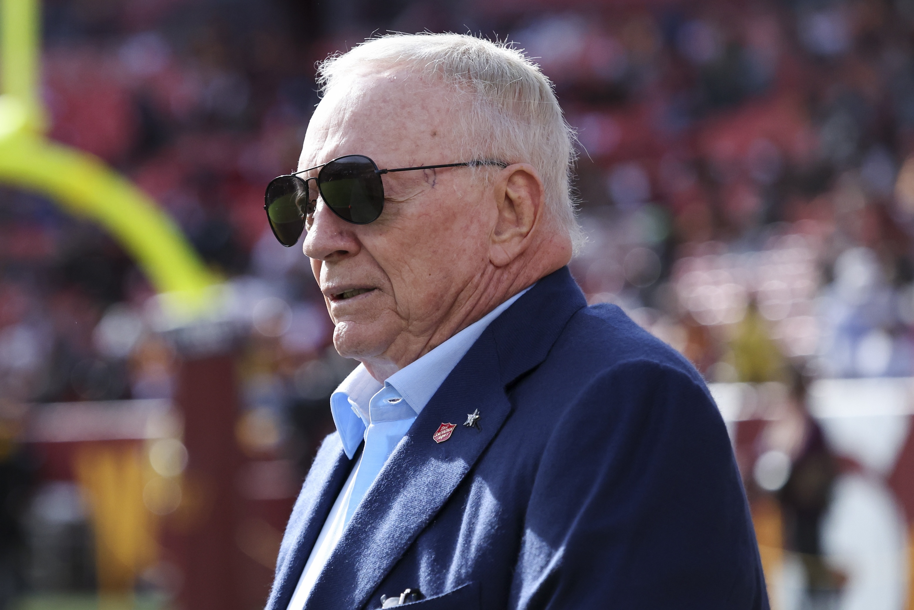 Jerry Jones, owner of the Dallas Cowboys, is seen on the field prior to a game against the Washington Commanders. His sunglasses are sitting in kind of a weird way, like hovering above his nose.