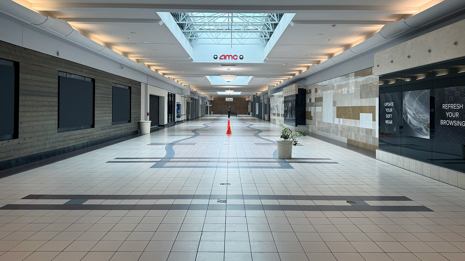 A long white mall hallway with empty storefronts and a sign for an AMC movie theater in the distance