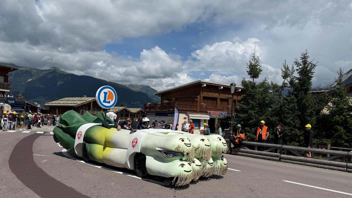 A parade float shaped like a big bundle of leeks, with smiley faces at their root ends.