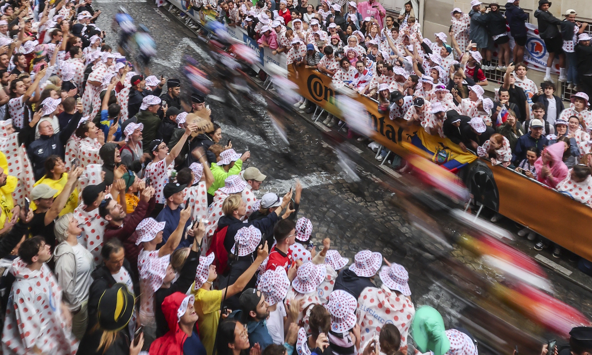 Tour de France riders pass as a blur of color through a narrow cobbled pass between throngs of fans on the Rue Lepic during the final stage of the 2025 Tour de France