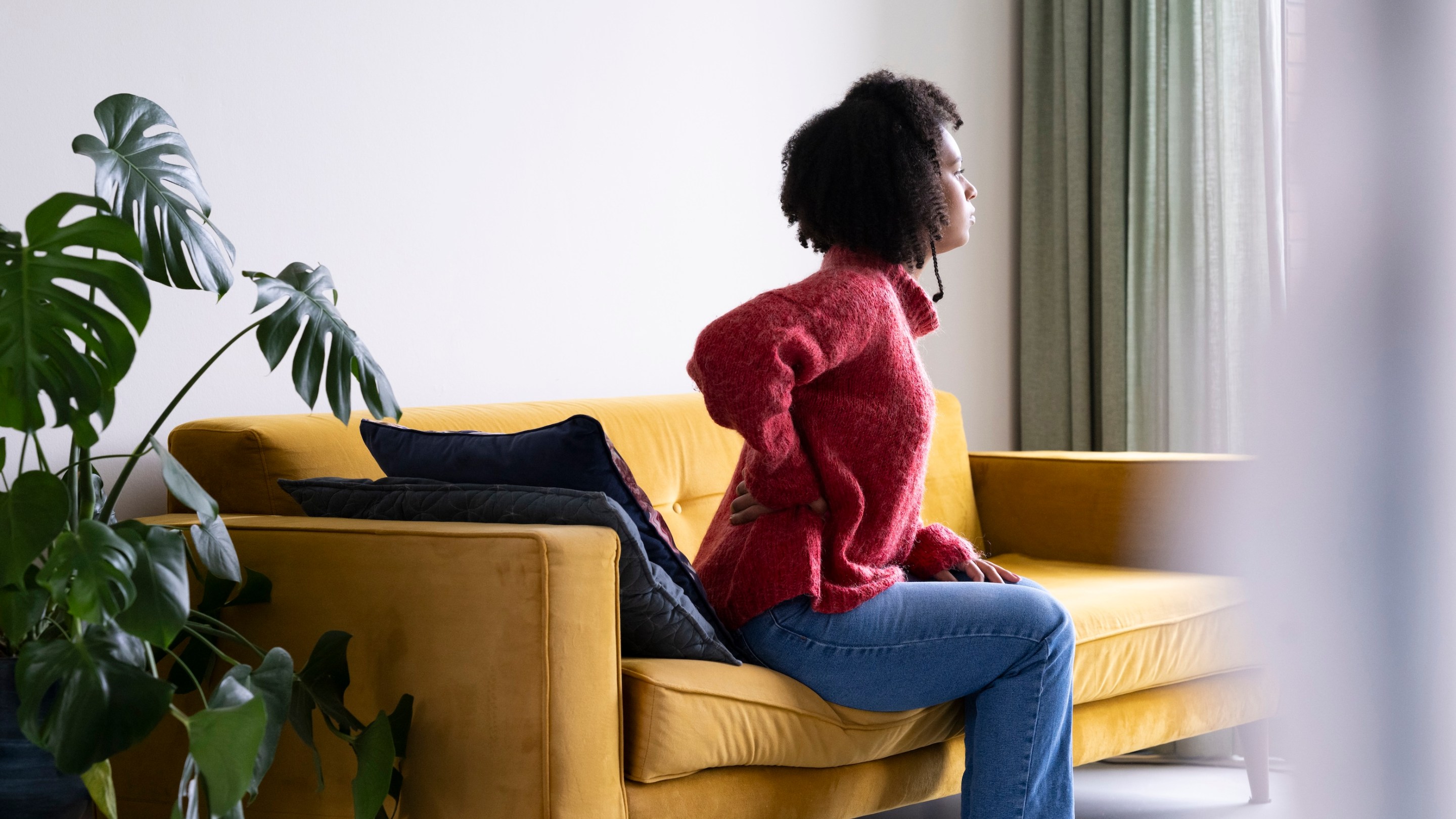 A young woman at home, feeling sick. She is, appropriately, holding her lower back.