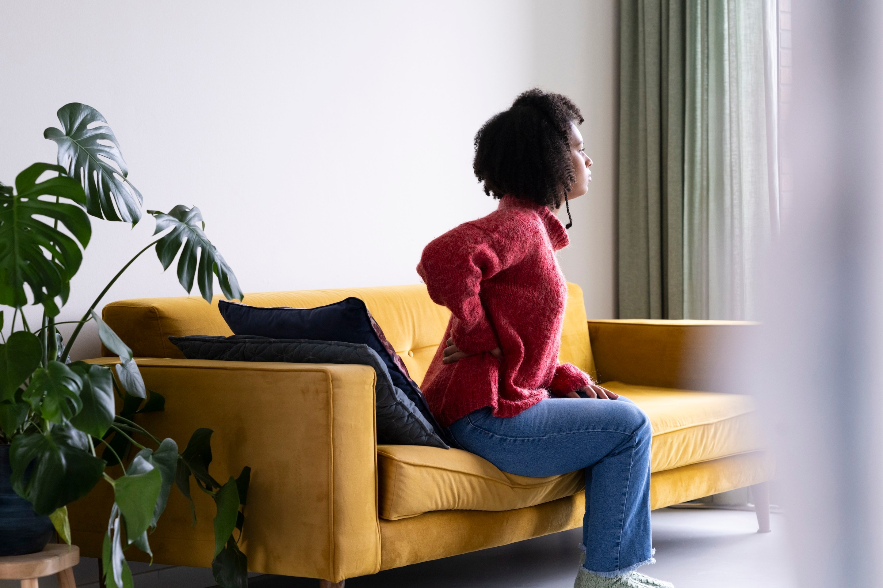 A young woman at home, feeling sick. She is, appropriately, holding her lower back.