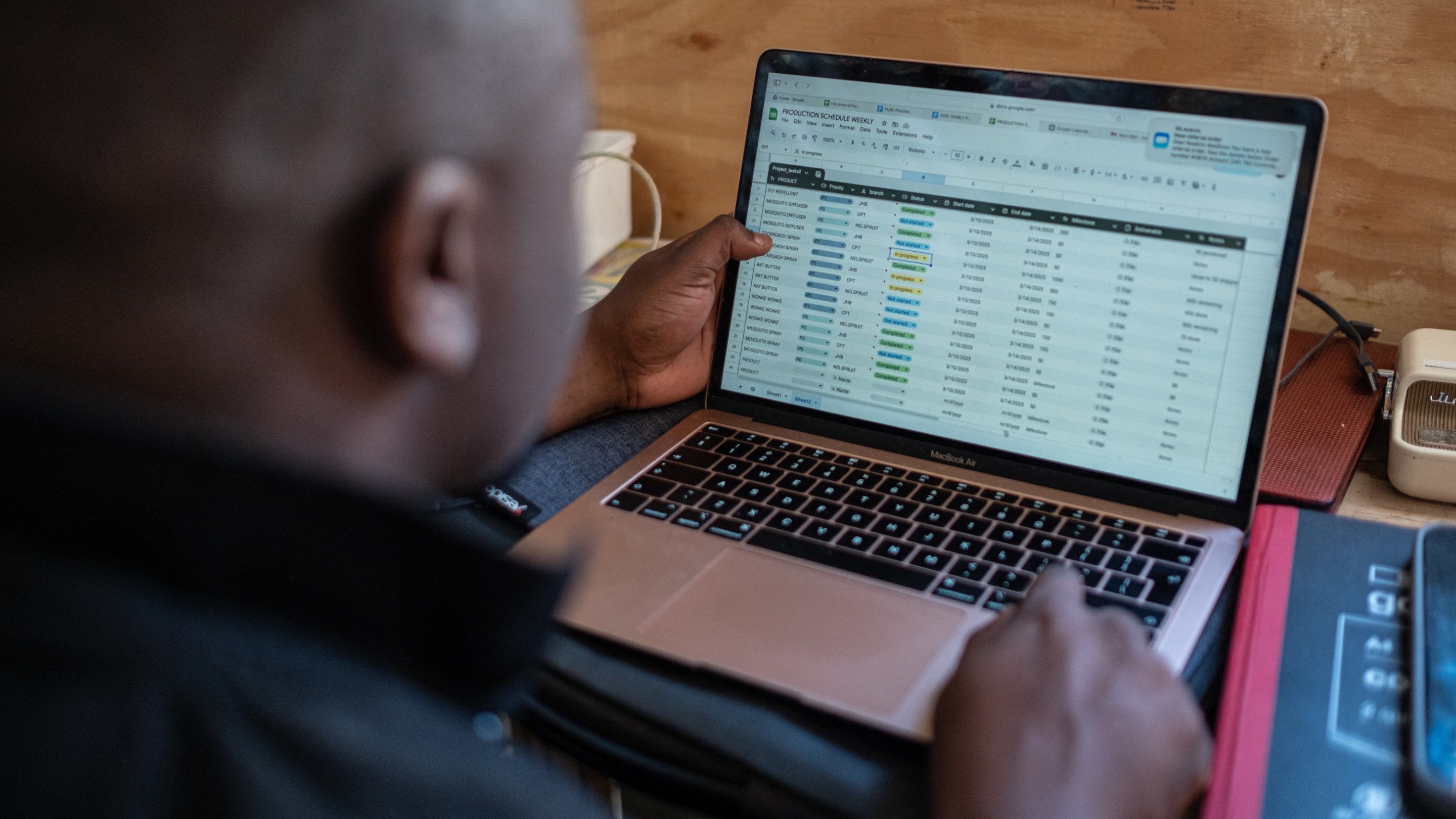 Kwakho Madikwain, associate of former gang member Nicholas Mnguni, fills out a spreadsheet of purchase orders in Khayelitsha on March 13, 2025. Former gang member Nicholas Mnguni, known as Zwe in his township, left the 20 Men gang in 2017 to start his own business, producing and selling perfumes, cleaning products, and insect repellent. His business, ML Scents, has enabled him to employ 4 seasonal workers, with the hope of keeping them off the streets, and away from gang recruitment. As a former gangster, Nicholas is exempt from paying the protection fee demanded by local gangs. “Luckily, they know me, so they leave me alone, plus, I don’t want to be aggressive anymore,” he says. (Photo by EMMANUEL CROSET / AFP)