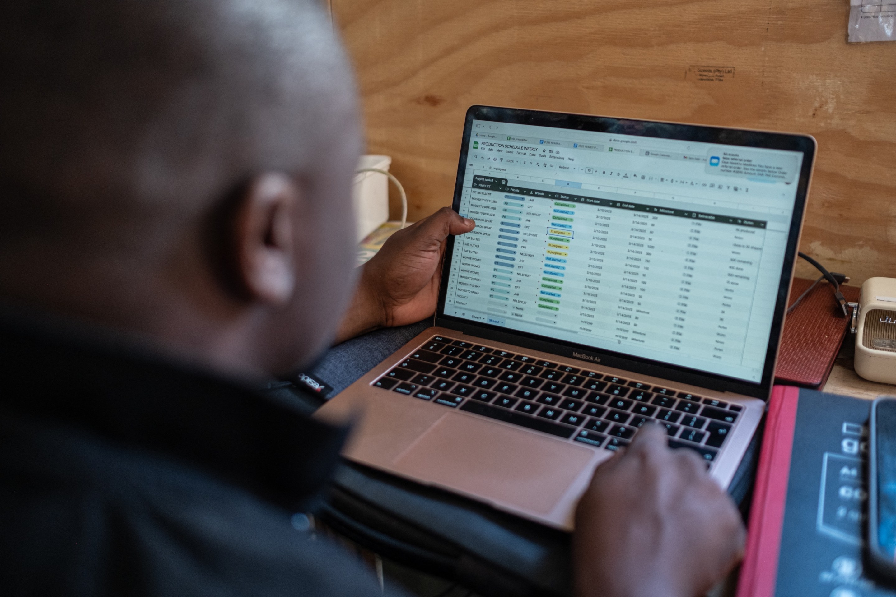 Kwakho Madikwain, associate of former gang member Nicholas Mnguni, fills out a spreadsheet of purchase orders in Khayelitsha on March 13, 2025. Former gang member Nicholas Mnguni, known as Zwe in his township, left the 20 Men gang in 2017 to start his own business, producing and selling perfumes, cleaning products, and insect repellent. His business, ML Scents, has enabled him to employ 4 seasonal workers, with the hope of keeping them off the streets, and away from gang recruitment. As a former gangster, Nicholas is exempt from paying the protection fee demanded by local gangs. “Luckily, they know me, so they leave me alone, plus, I don’t want to be aggressive anymore,” he says. (Photo by EMMANUEL CROSET / AFP)