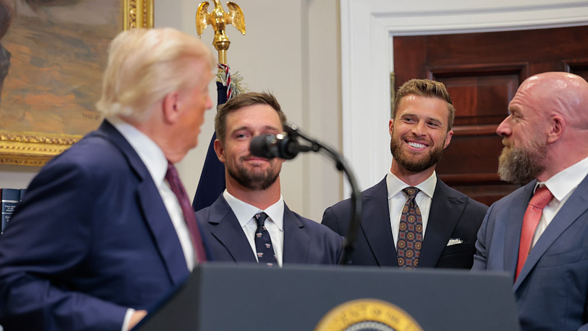 U.S. President Donald Trump looks at (L-R) golfer Bryson DeChambeau, Kansas City Chiefs kicker Harrison Butker, and WWE Chief Creative Officer Paul “Triple H” Levesque as he speaks during an executive order signing ceremony in the Roosevelt Room of the White House on July 31, 2025 in Washington, DC. Trump signed a series of orders that will expand on his council on sports, fitness and nutrition, including by reviving the Presidential Fitness Test in public schools.